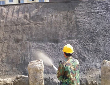 A worker is spraying cement to the slope with black sandblast hose.