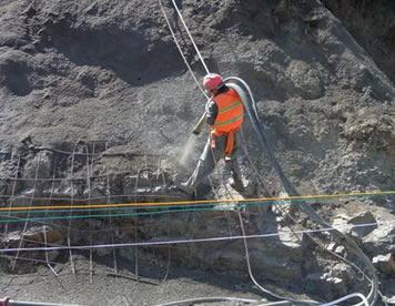 A worker standing on the slope is spraying cement to the slope with sandblast hose.