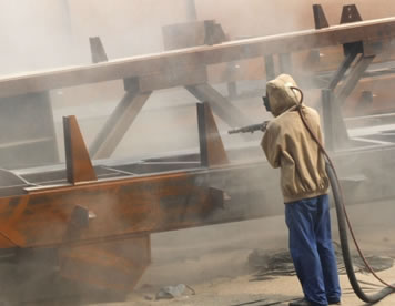 A worker is spraying sand to ship with sandblast hose.