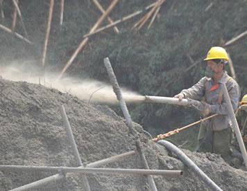 Two workers are spraying cement to the slope with sandblast hose.