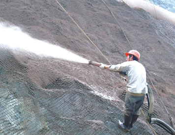 A worker standing on the slope is spraying cement to the slope with sandblast hose.